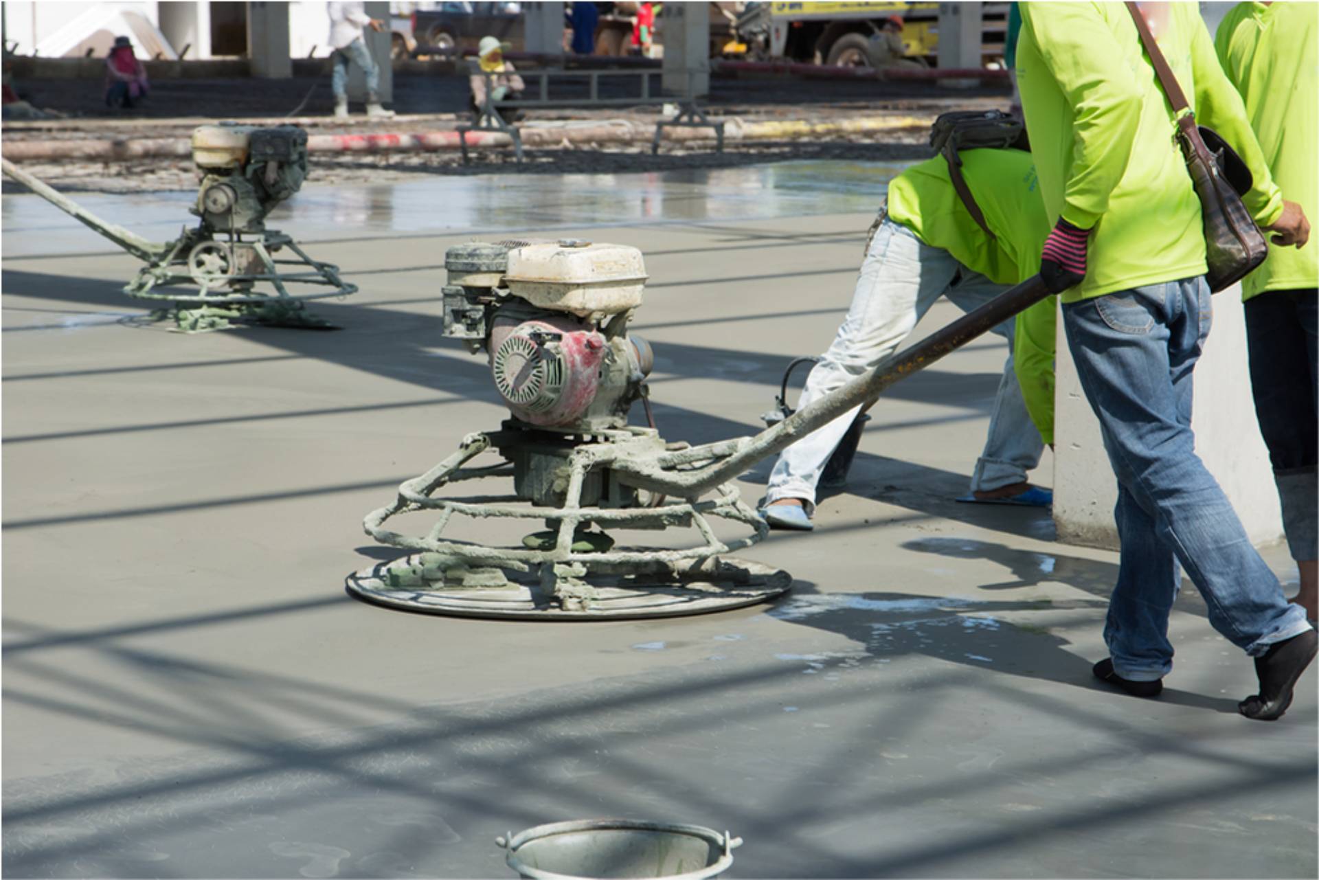 workers using a machine to spread concrete and flatten